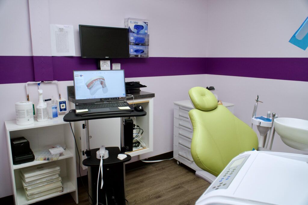 Treatment room with a green dental chair, digital scanner, and laptop showing a 3D model of teeth